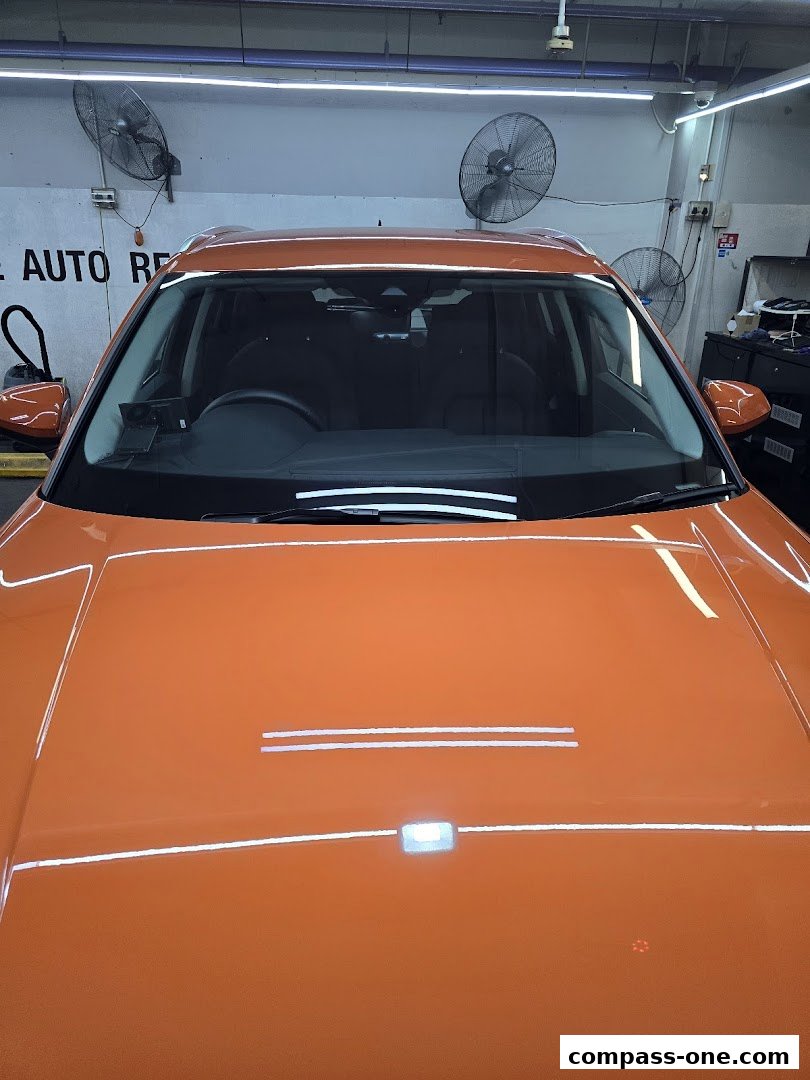 An orange car is parked inside a workshop with fans on the wall.