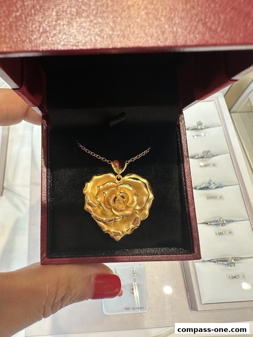 A hand holds a gold rose pendant in a jewelry box, with rings displayed in the background.