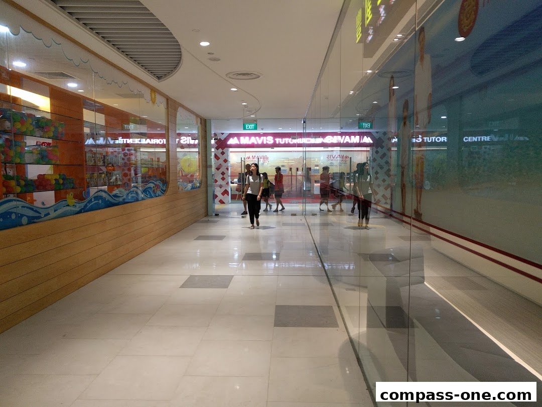 A bright shopping mall corridor with a Mavis Tutorial shop entrance and reflections in the glass.