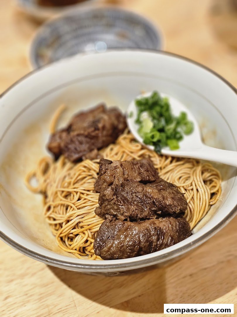 A close-up shot of a bowl of noodles with tender braised beef and chopped scallions.