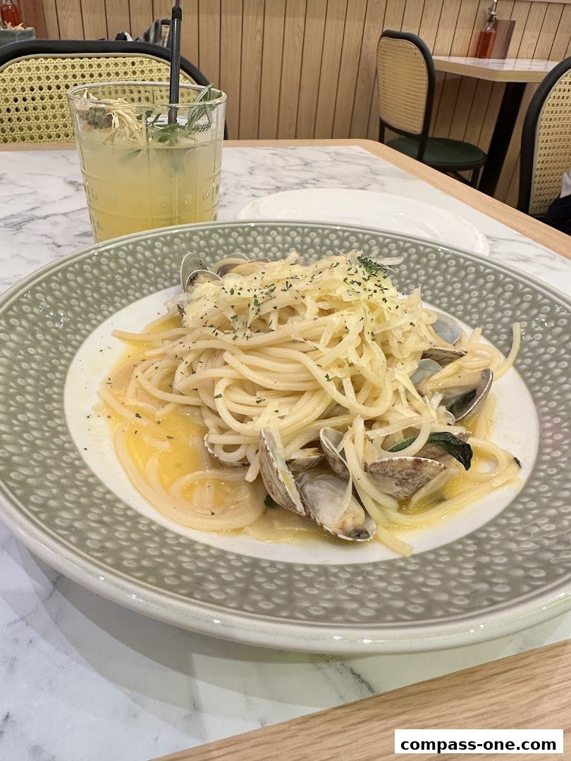 A plate of spaghetti with clams and a refreshing drink on a marble table.