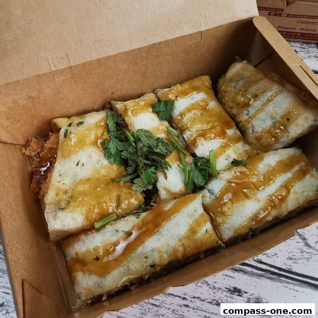 A box of Shihlin Taiwan Street Snacks' signature fried snacks drizzled with sauce and garnished with cilantro.