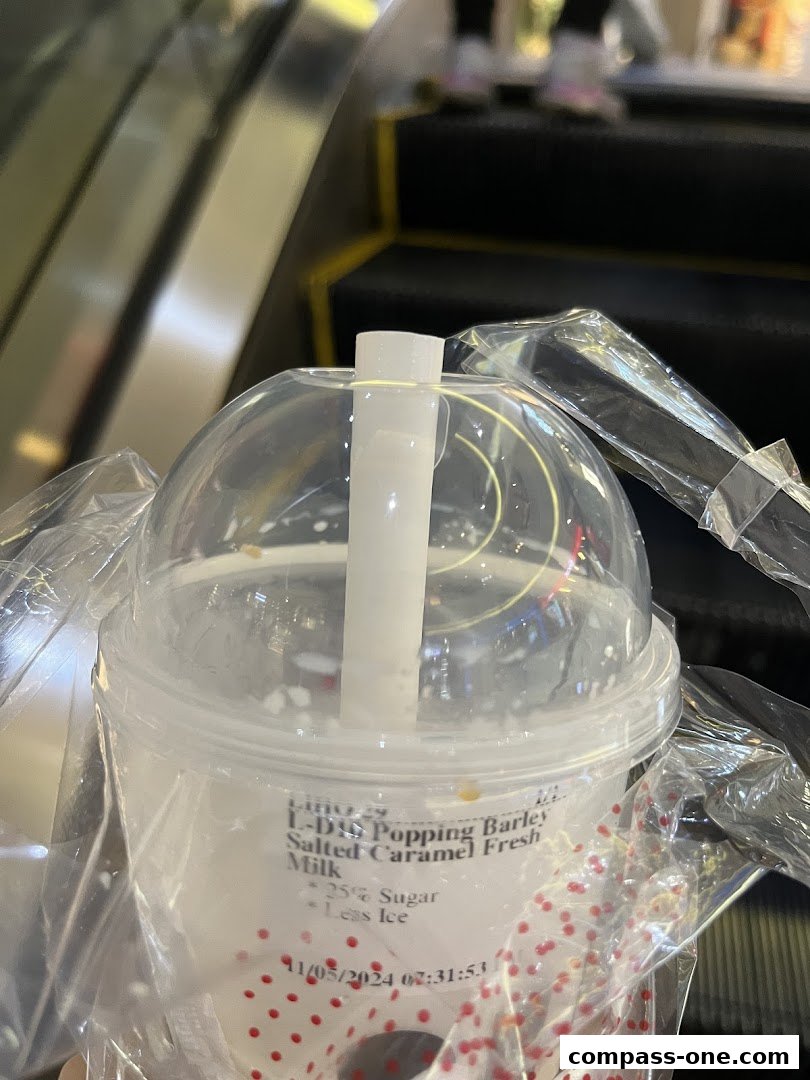 A close-up of a LiHO TEA drink with a straw on an escalator.