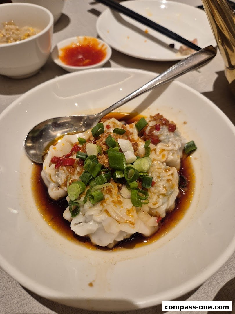 A close-up of wontons in chili oil, garnished with scallions and chili flakes.