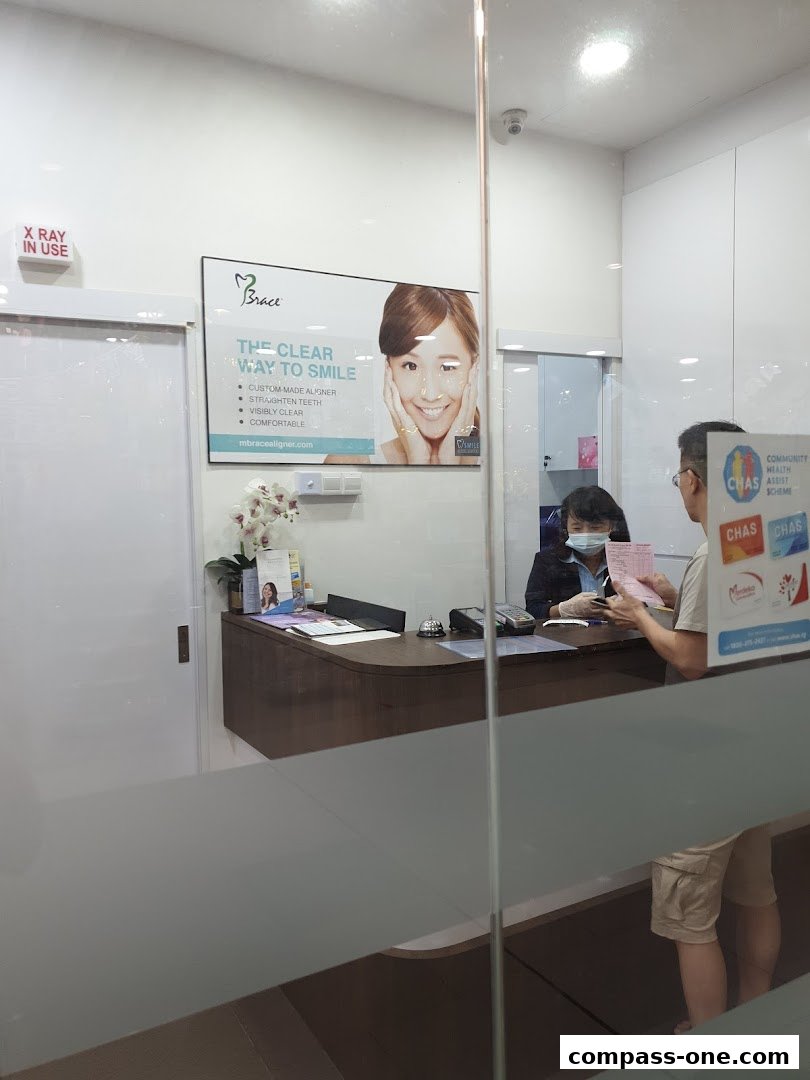 A dental clinic reception area with staff and a patient at the counter.