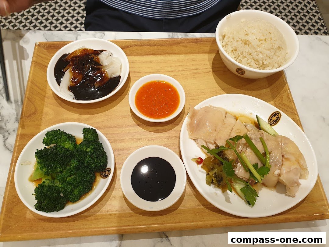 A delicious plate of Hainanese chicken rice with steamed broccoli and dipping sauces.