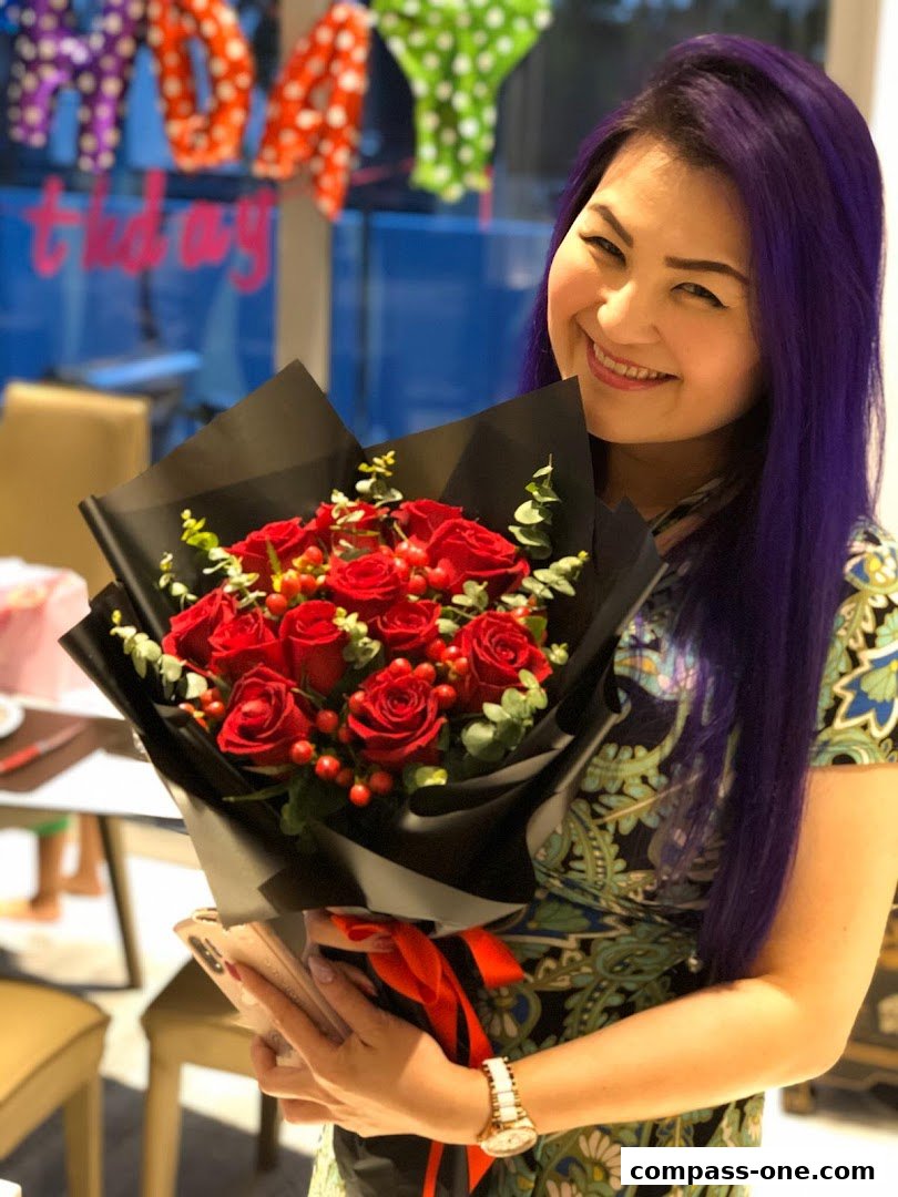 A smiling woman with purple hair holds a bouquet of red roses.