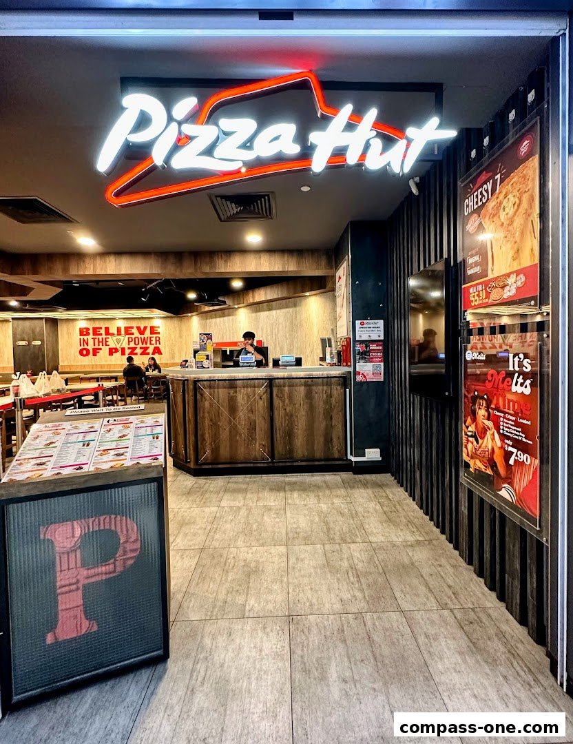 The entrance to a Pizza Hut restaurant with its iconic neon sign and promotional posters.