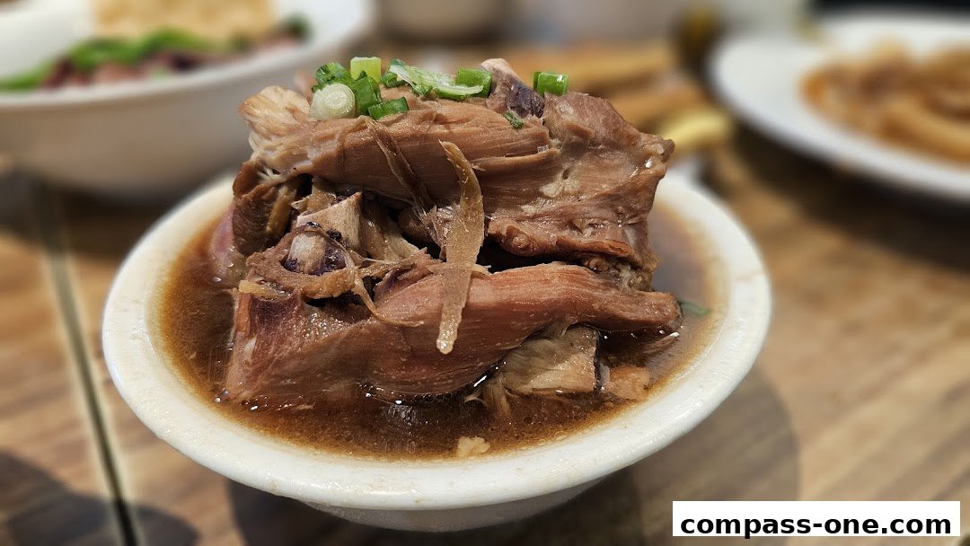 A close-up of a bowl of tender braised meat with broth and garnished with chopped green onions.