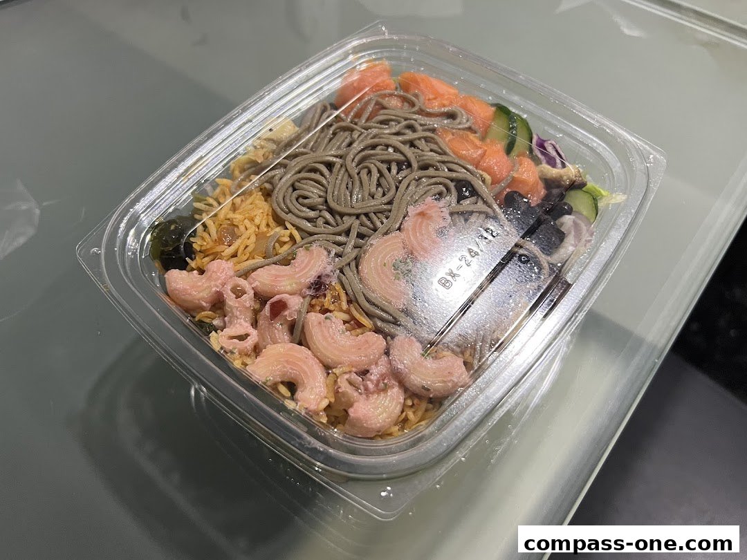 A clear plastic container filled with a colorful and diverse meal, featuring noodles, rice, salmon, and pasta.
