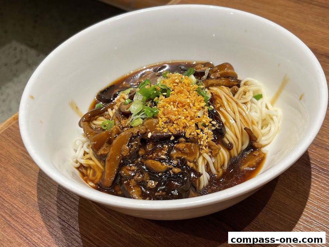 A bowl of noodles with mushrooms and sauce, garnished with green onions and crispy bits.