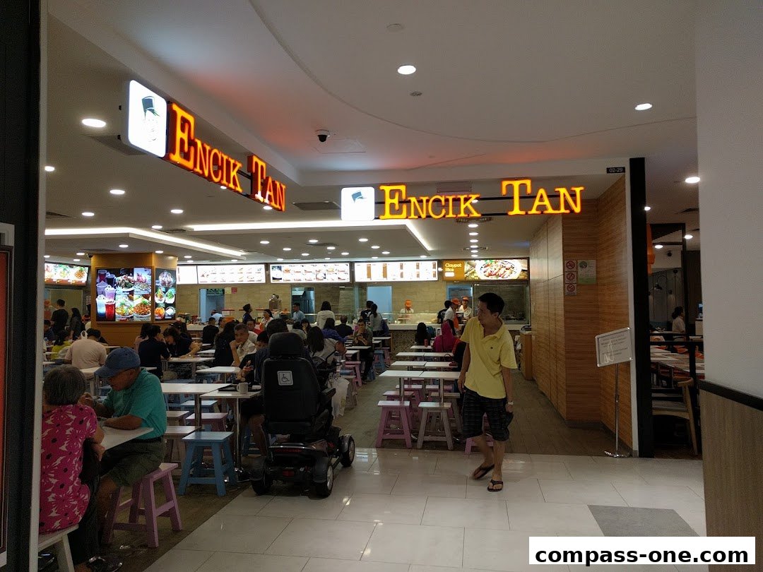 A busy food court with people dining at tables and the Encik Tan restaurant signage visible.