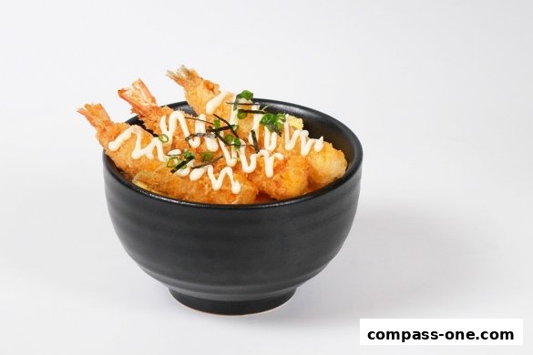 A black bowl filled with crispy fried shrimp, rice, and drizzled with mayonnaise.