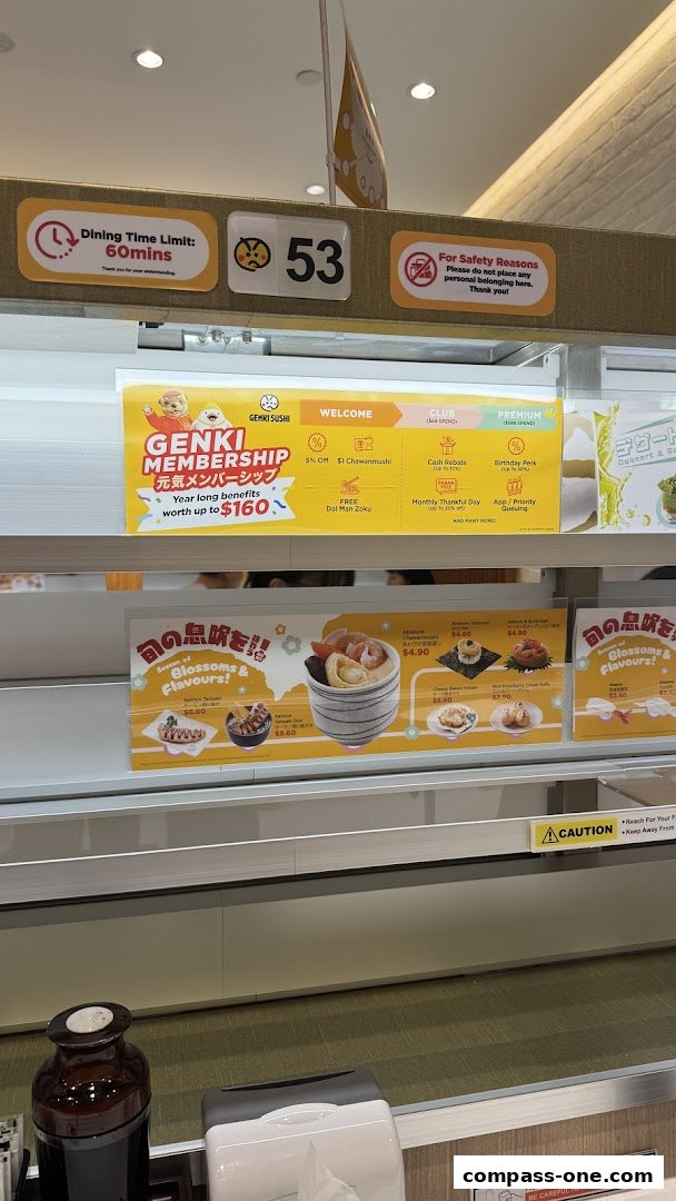 Genki Sushi restaurant interior with a conveyor belt and promotional signs for membership and seasonal dishes.