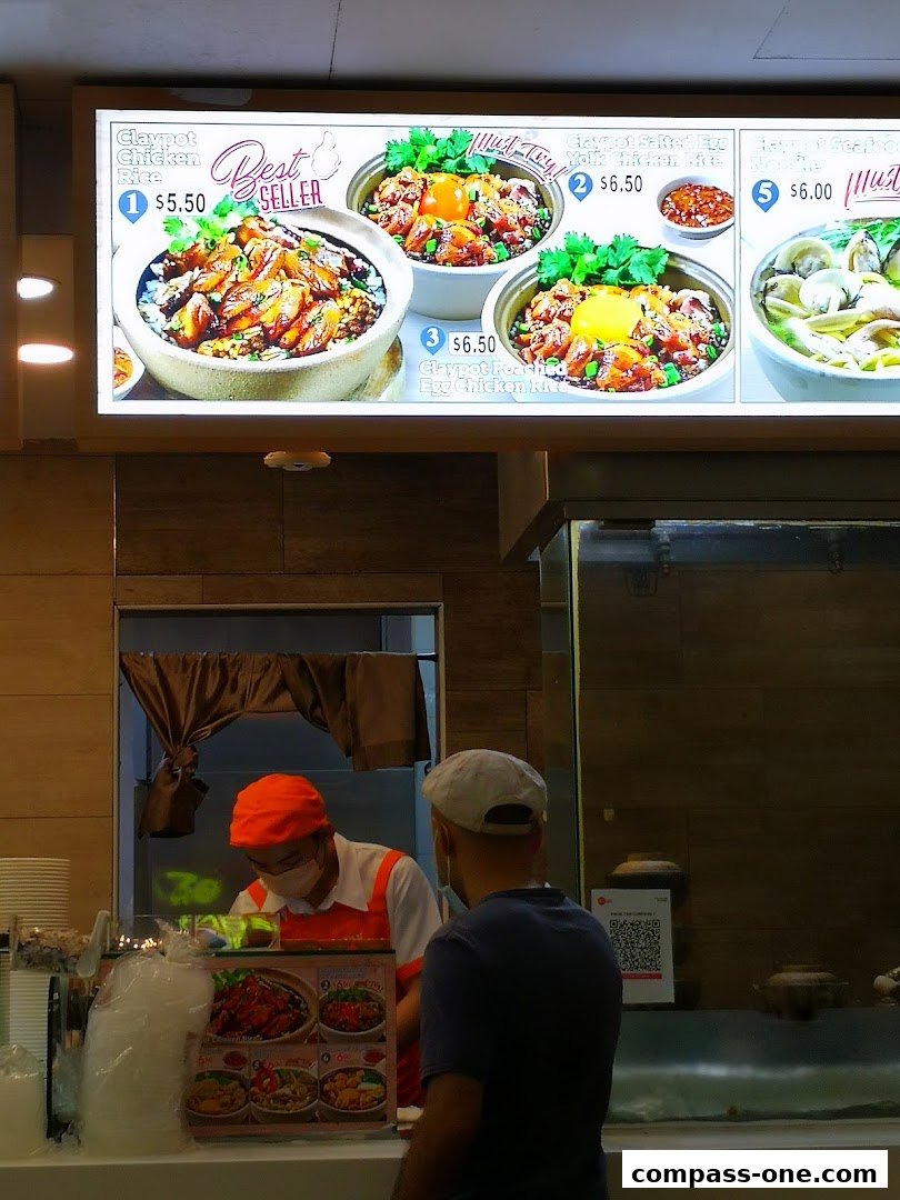 A brightly lit menu board displays various claypot rice dishes with prices and enticing images.