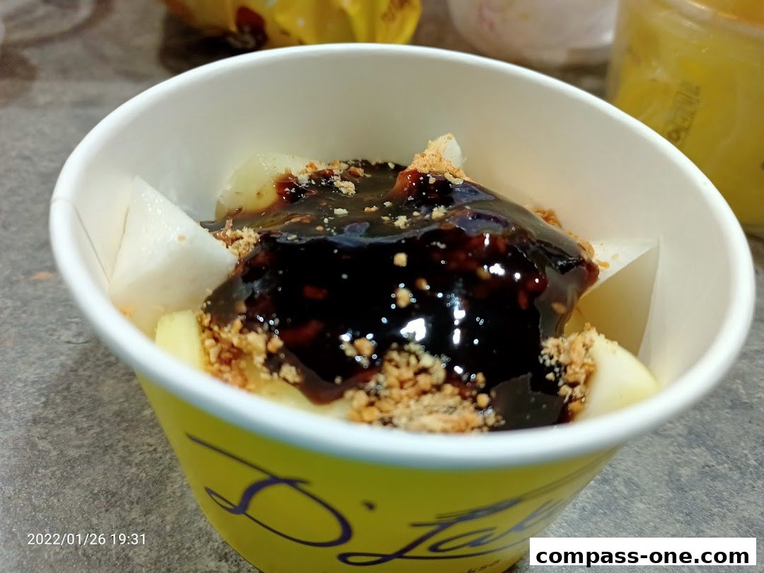 A cup of fruit salad with a dark sauce and crushed peanuts.
