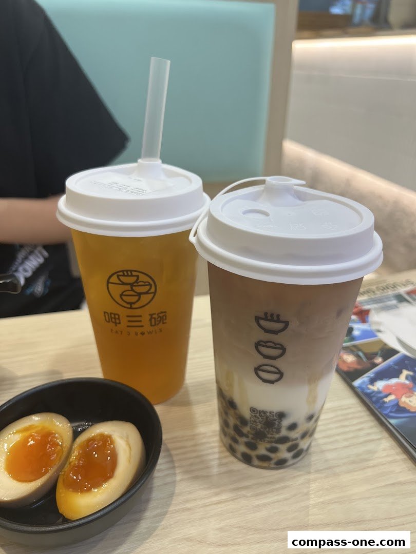 Two drinks and a bowl of braised eggs on a wooden table at Eat 3 Bowls.