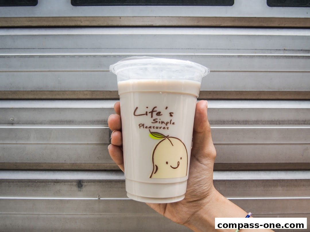 A hand holds a plastic cup with a creamy beverage and a cute peach logo.