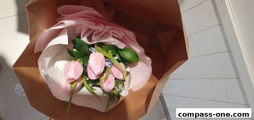 A bouquet of pink tulips and greenery is presented in a brown paper bag.