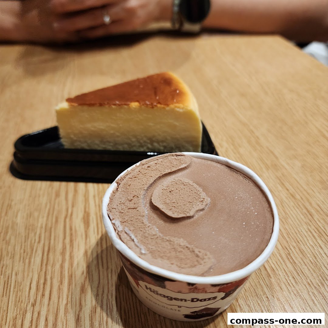 A slice of cheesecake and a cup of Häagen-Dazs chocolate ice cream on a wooden table.