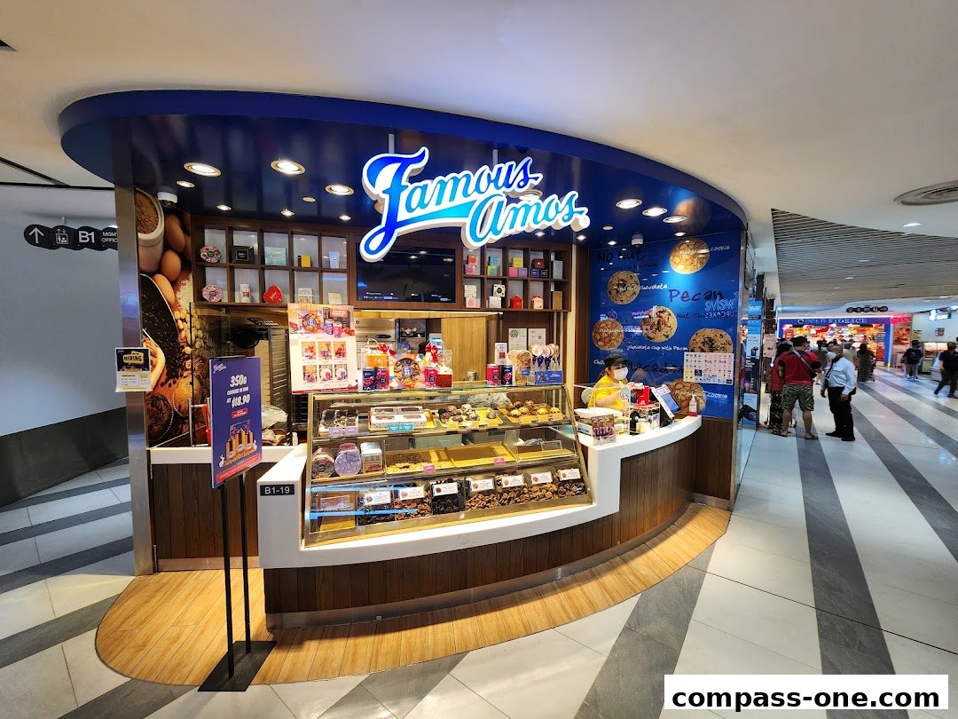 A Famous Amos cookie shop with a display of cookies and a staff member serving customers.