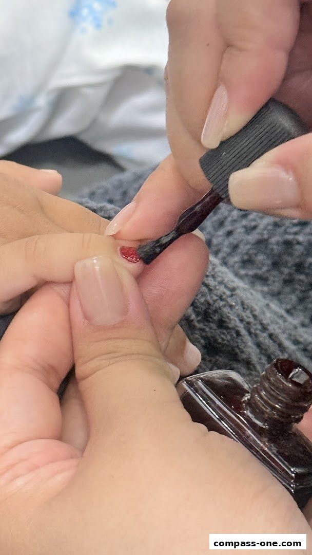 A close-up shot of a nail technician applying dark red nail polish to a client's fingernail.
