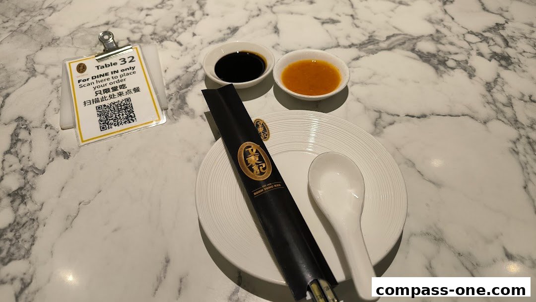 A table setting at Boon Tong Kee with chopsticks, spoon, dipping sauces, and a QR code for ordering.