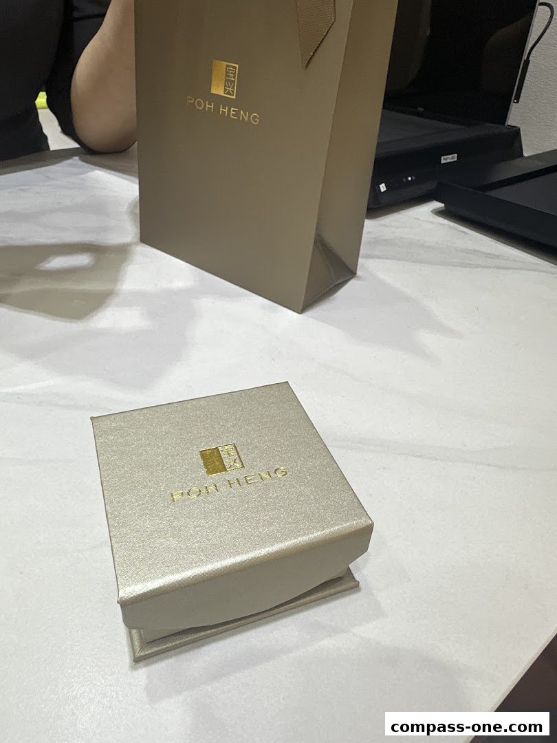 A Poh Heng Jewellery gift box and shopping bag on a marble surface.