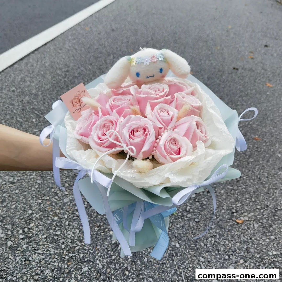 A hand holds a bouquet of pink roses with a plush toy on top.