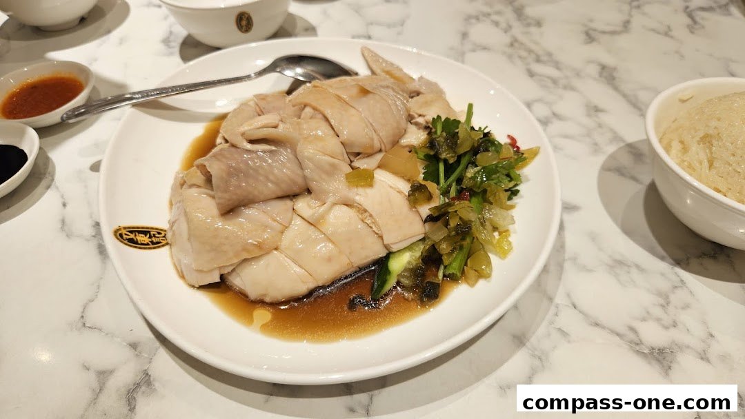A plate of delicious Hainanese chicken rice with side dishes and a bowl of rice.