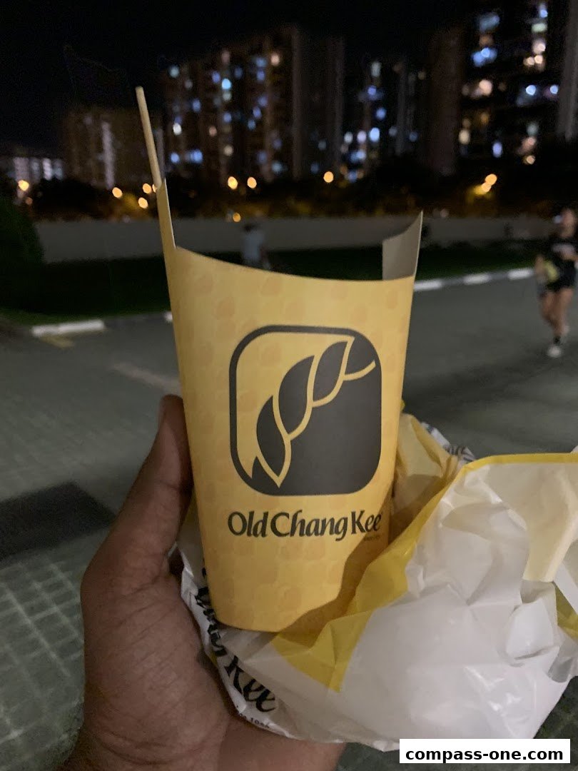 A hand holds a branded Old Chang Kee paper container with a plastic bag.
