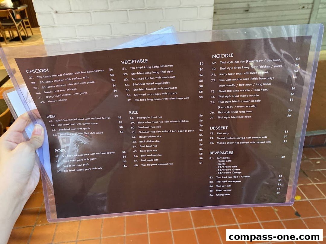 A person holding a menu from Nakhon Kitchen, displaying various Thai dishes and beverages.