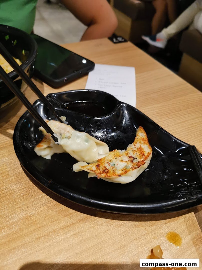 A plate of pan-fried dumplings being picked up with chopsticks, with a receipt and phone on the table.