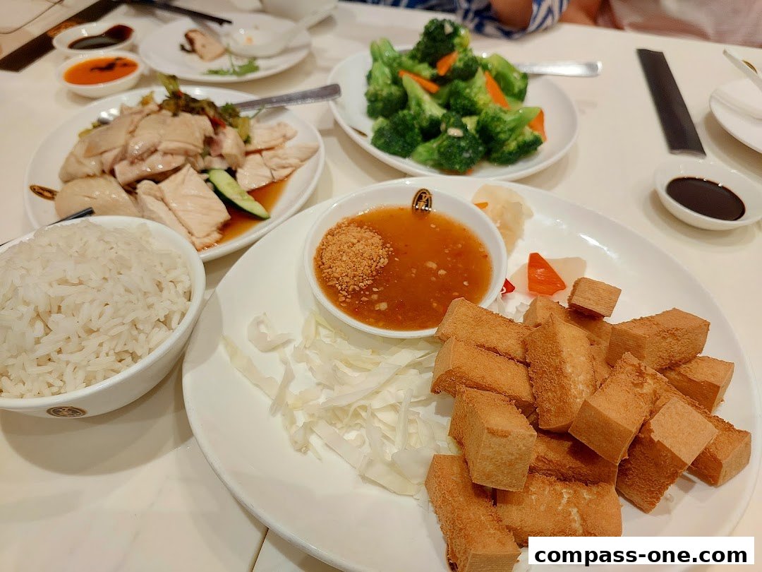 A table laden with delicious dishes, including Hainanese chicken rice, fried tofu, and steamed vegetables.