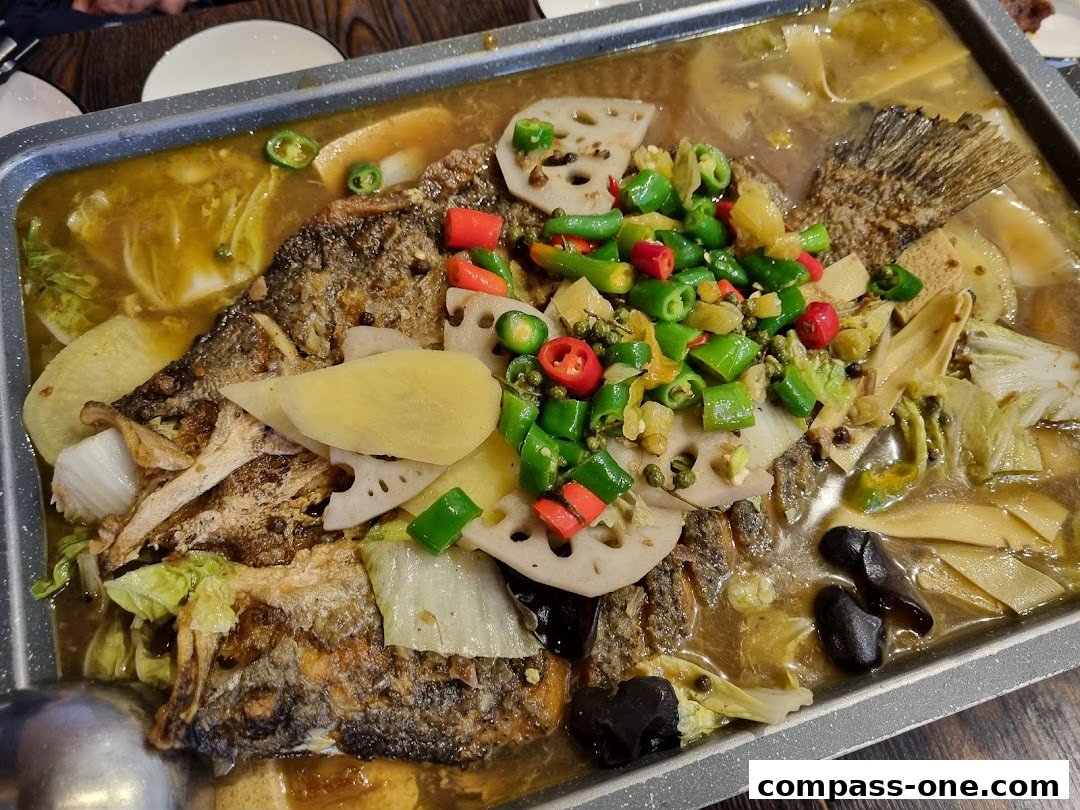 A close-up of a grilled fish dish with chili peppers, lotus root, and vegetables in a savory broth.