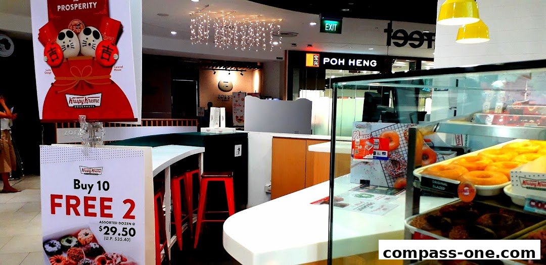 A Krispy Kreme shop interior with display cases full of donuts and promotional signage.