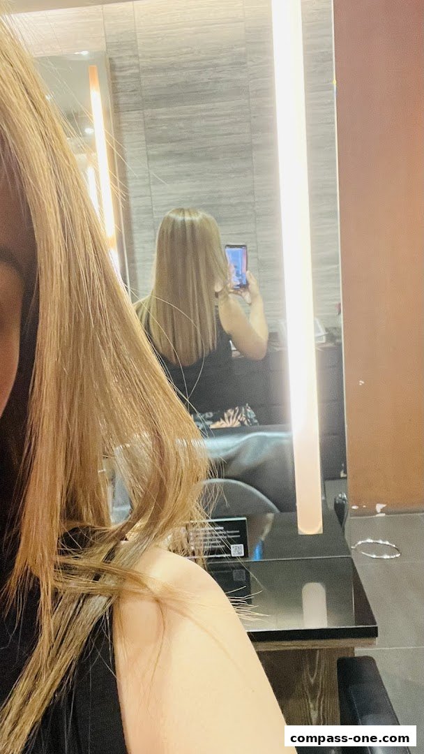 A woman with blonde hair takes a selfie in a salon mirror, showing her new hairstyle.