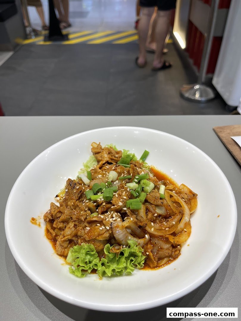 A close-up of a Korean street food dish with meat, onions, and lettuce in a white bowl.
