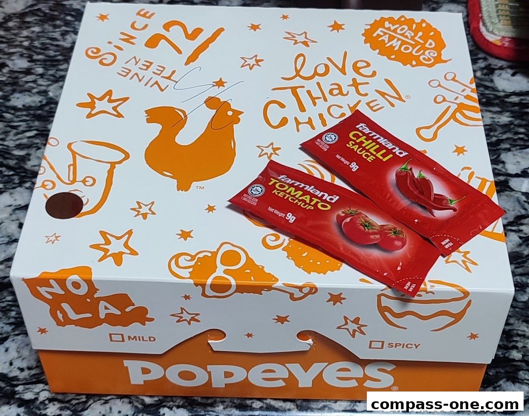A Popeyes chicken box with two sauce packets and festive designs.
