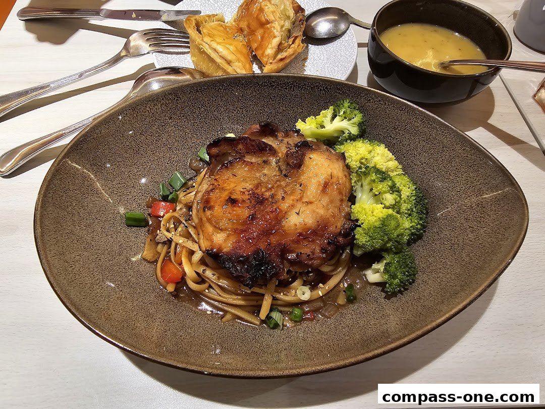 A delicious meal featuring grilled chicken, noodles, broccoli, and a side of soup.
