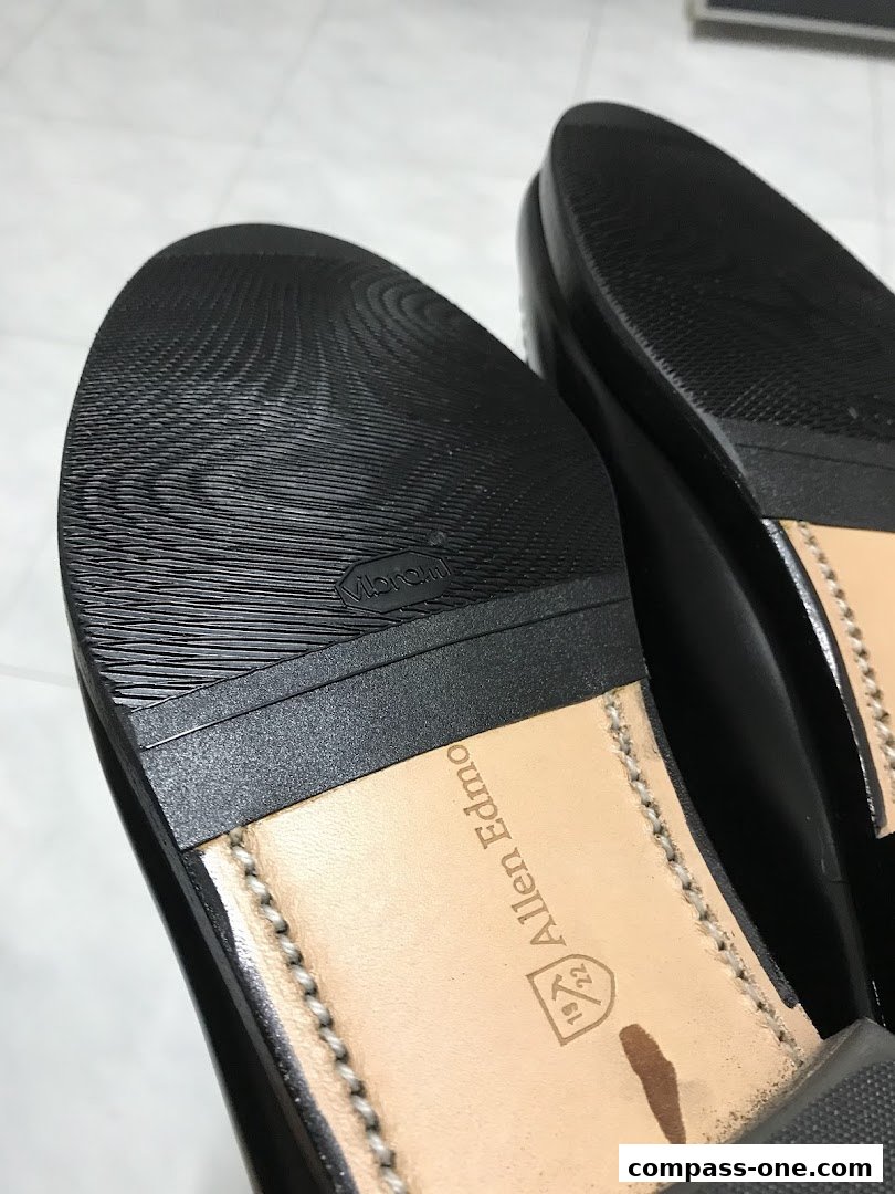 Close-up view of the soles of two black leather shoes, showing brand details.