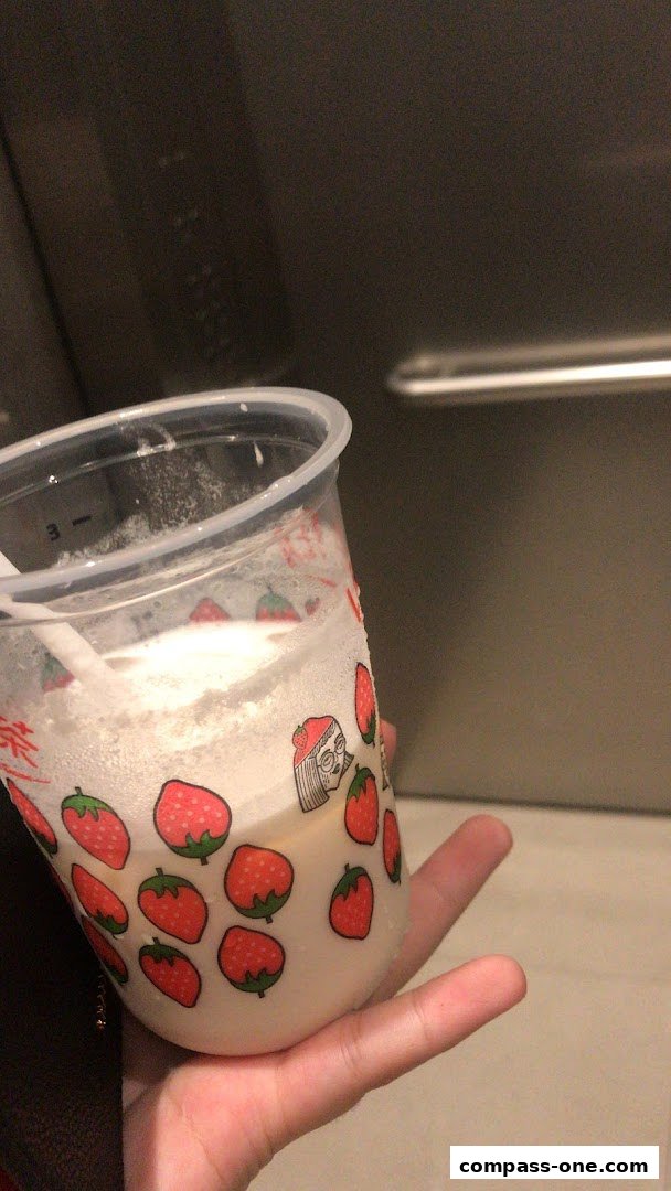 A hand holds a LiHO TEA cup with strawberry designs and a white beverage.