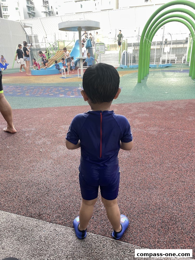 A child in a blue swimsuit stands on a wet, red surface at a water park.