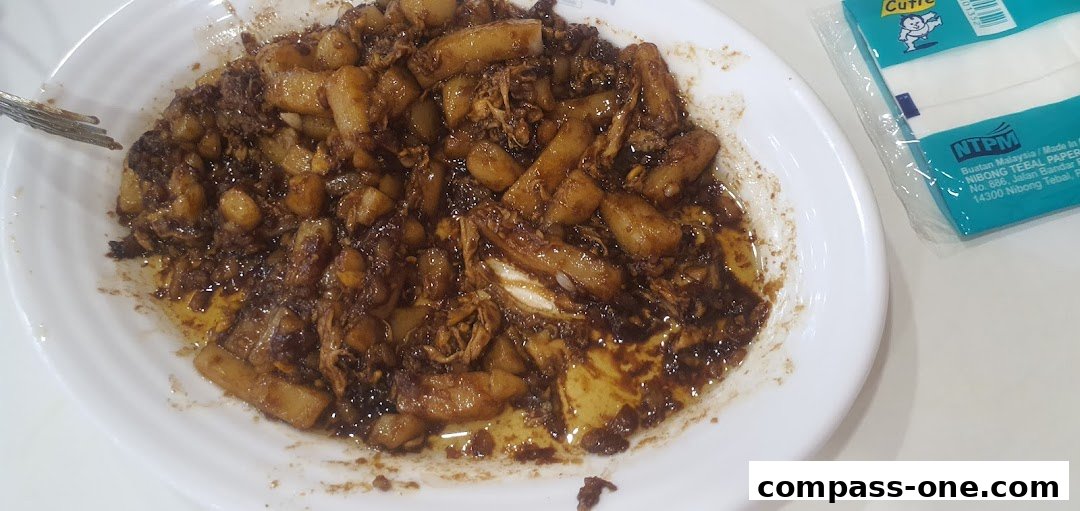 A close-up of a white plate filled with a savory dish, possibly noodles or rice cakes, in a dark sauce.