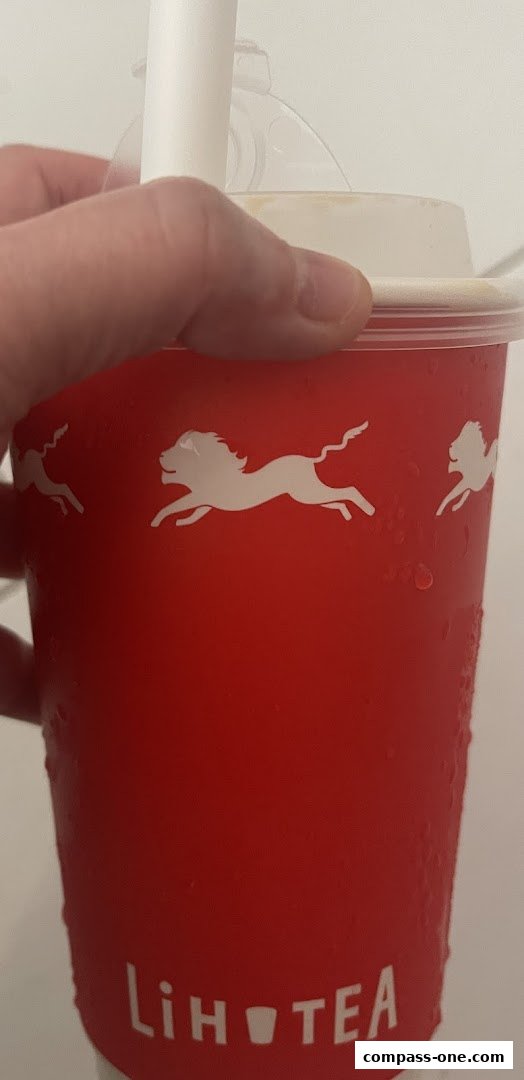 A hand holds a red LiHO TEA cup with white lion logos and condensation.