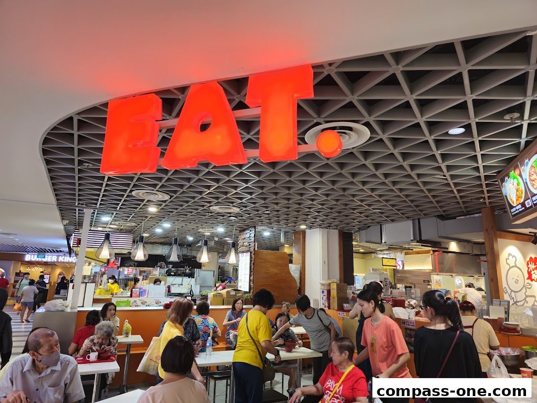 People dining at tables under a large red 'EAT' sign in a food court.
