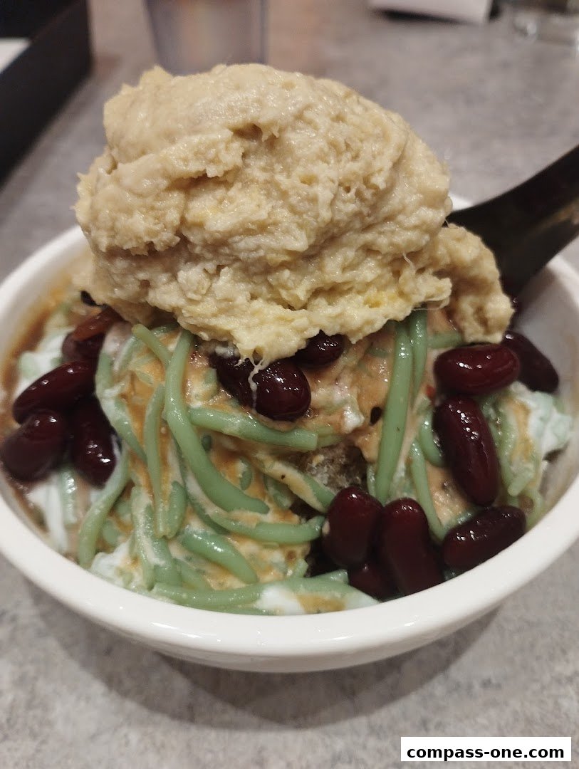 A close-up shot of a bowl of Cendol dessert with red beans and a scoop of durian paste.