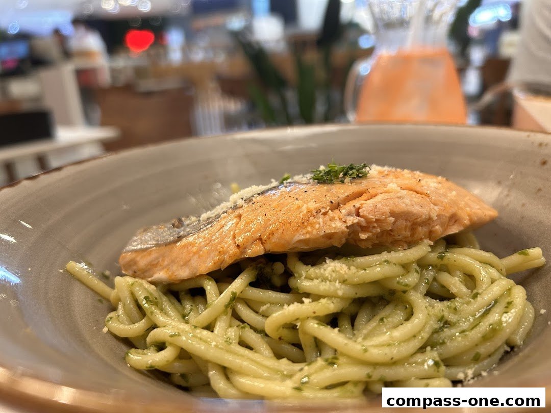 A close-up of a delicious pasta dish with a piece of salmon and a side of juice.