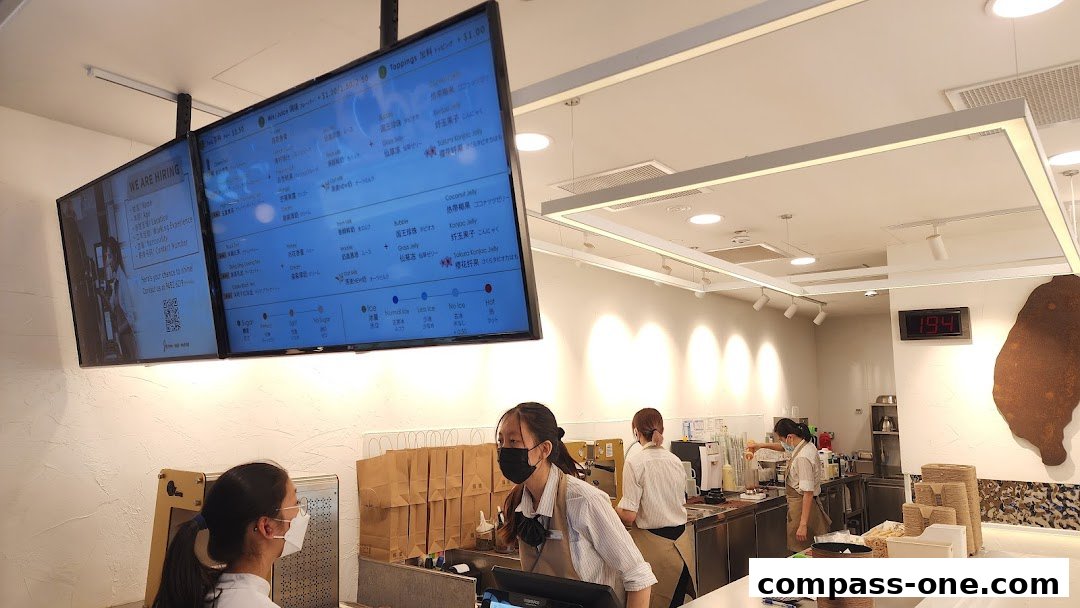 Staff members working behind the counter at CHICHA San Chen, with digital menus displaying drink options.