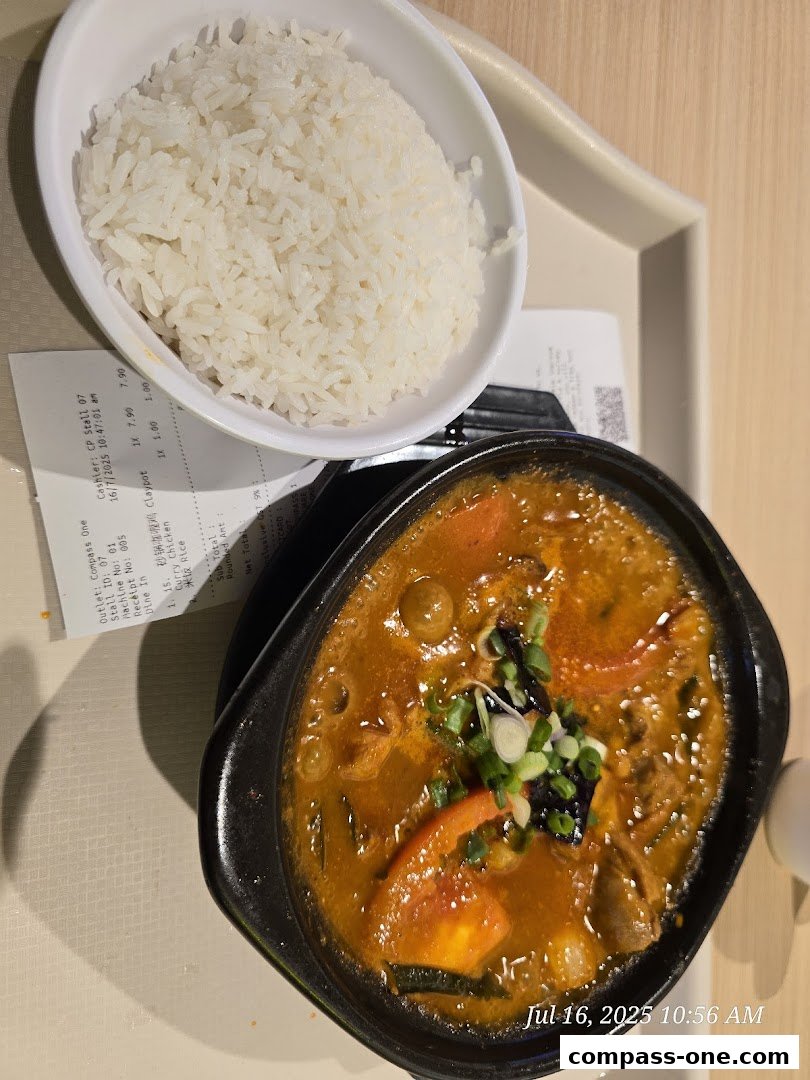 A close-up of a claypot dish with rice, featuring a rich orange sauce and garnished with green onions.